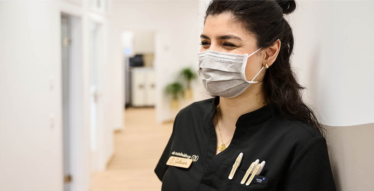 Eine Mitarbeiterin der Zahnarztpraxis zahnlieblinge in Nürnberg lacht unter ihrer Maske